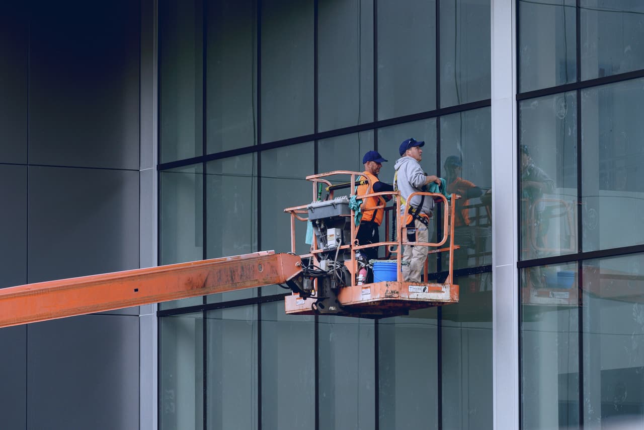 Two cleaners on a cherry picker cleaning an office glass facade